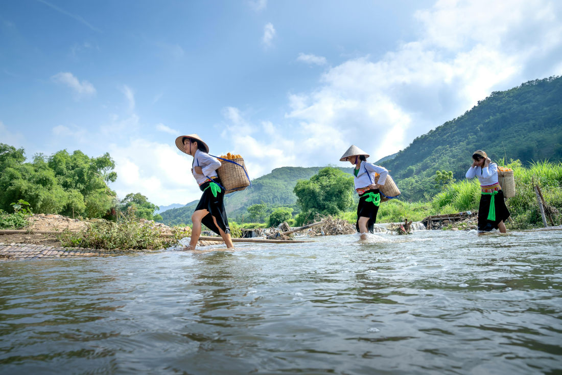 Asian women carrying baskets of vegetables accross a river